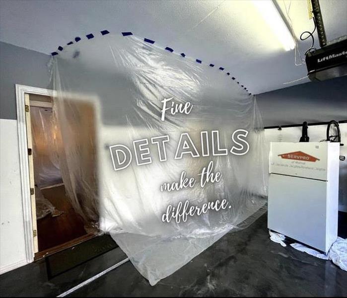 Plastic drop sheeting covers an open doorway in a greyish-blue garage. A refrigerator can be seen.